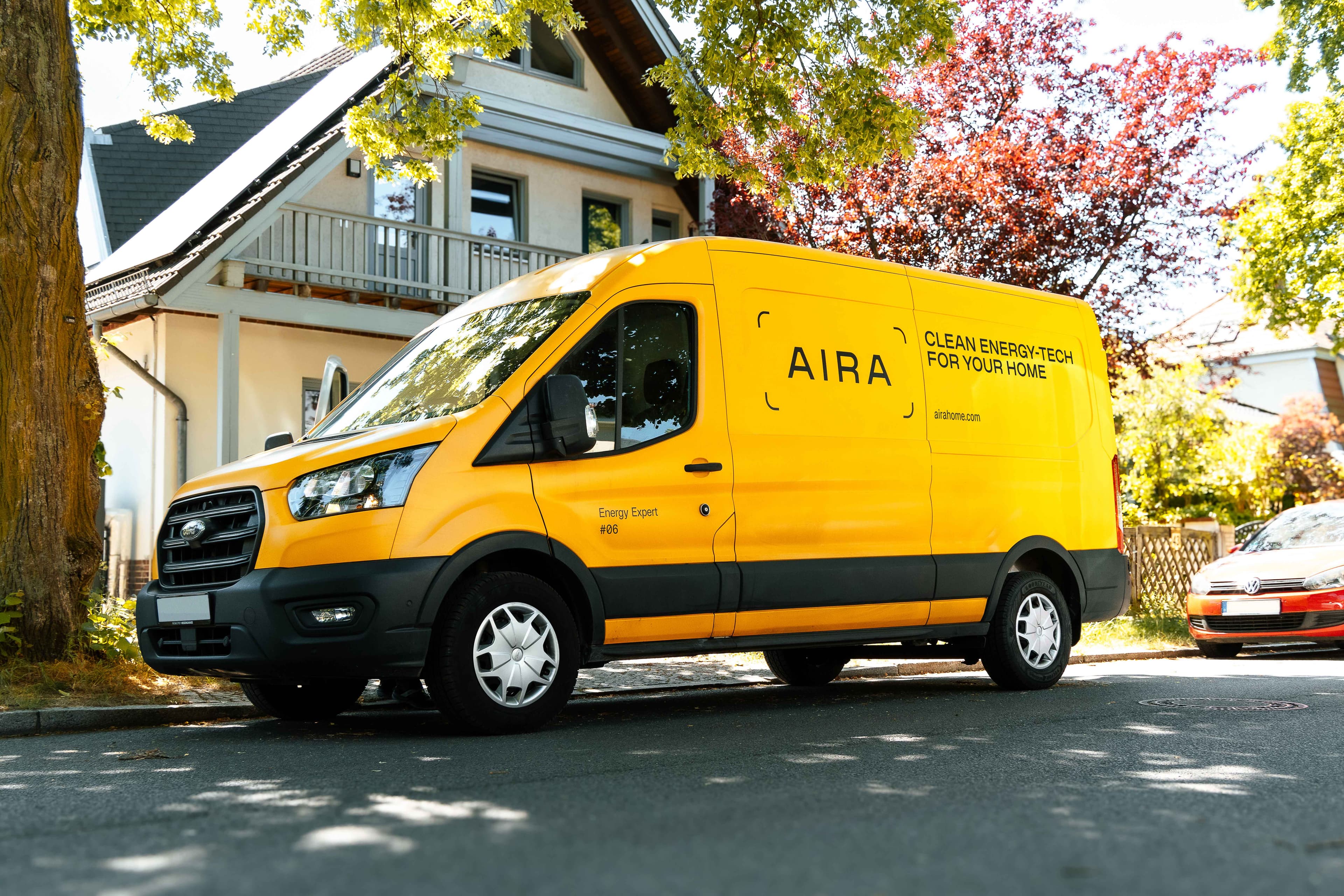 A yellow Aira branded van in front of an A-frame house surrounded by foliage