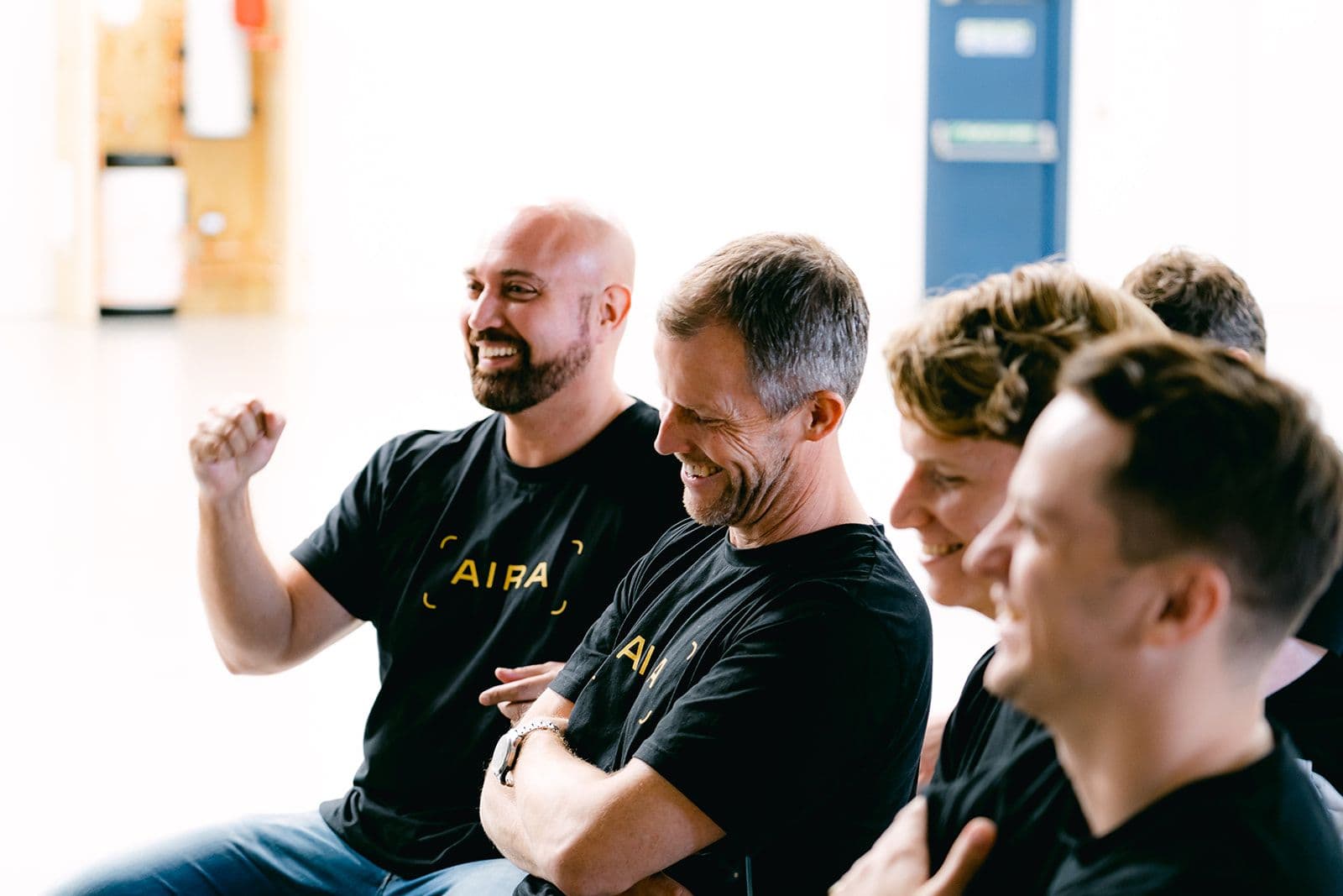 Aira staff sat in a row smiling with one employee with a triumphant fist up